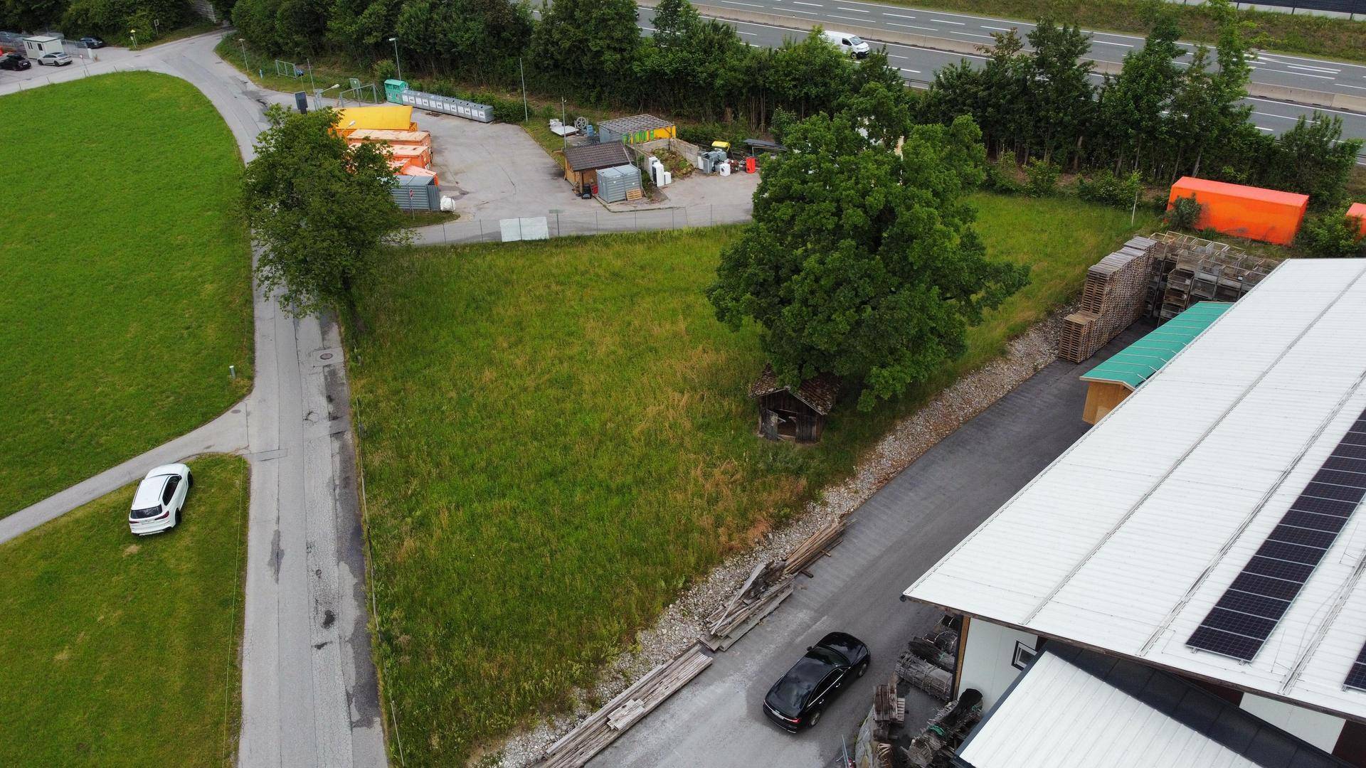 Übersichtliche Luftaufnahme eines dreieckigen Grundstücks mit Grasfläche, angrenzend an eine Straße und eine Autobahn.