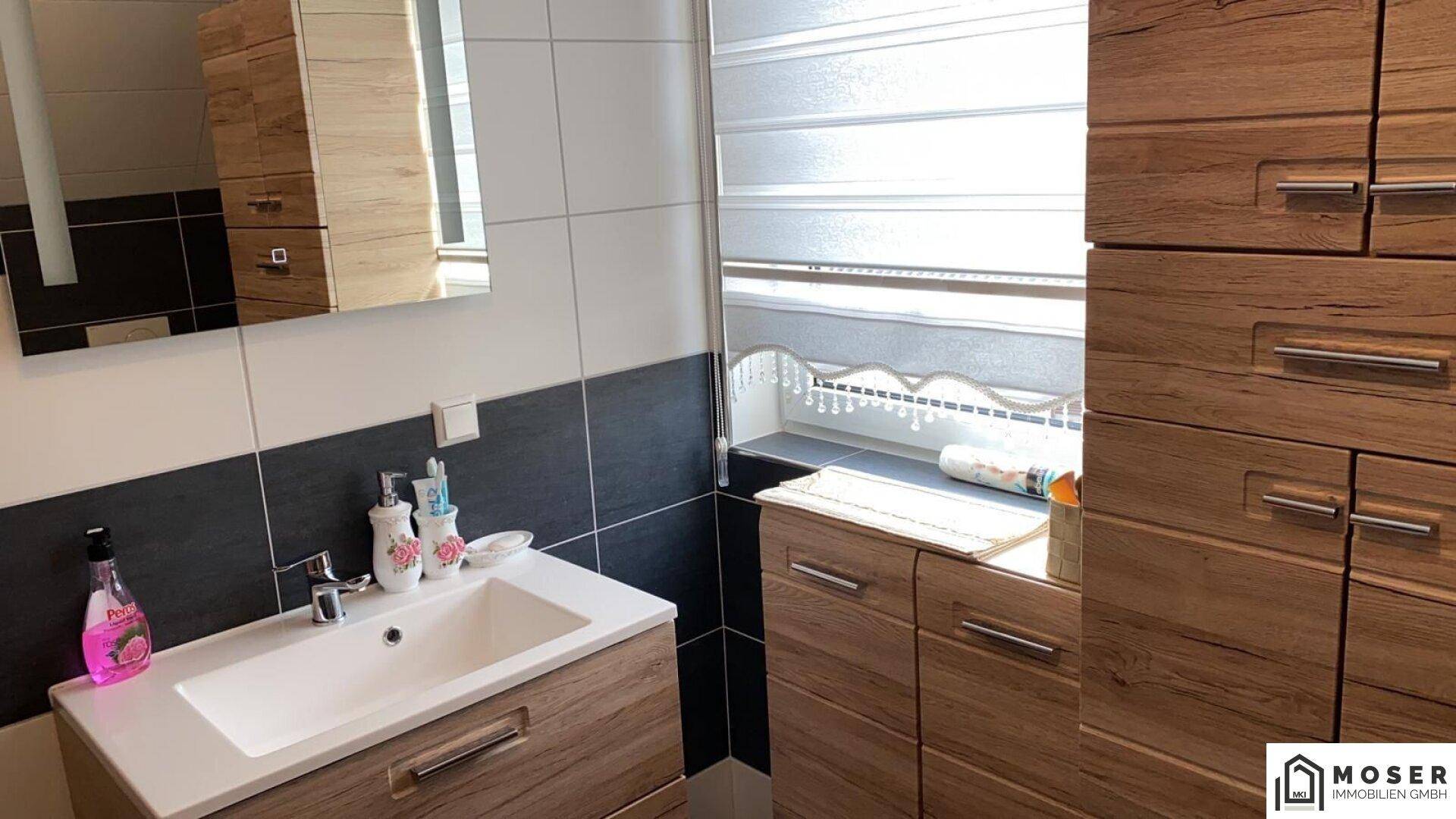 Modernes Badezimmer mit Holzoptik-Möbeln, Waschbecken und Spiegelschrank.