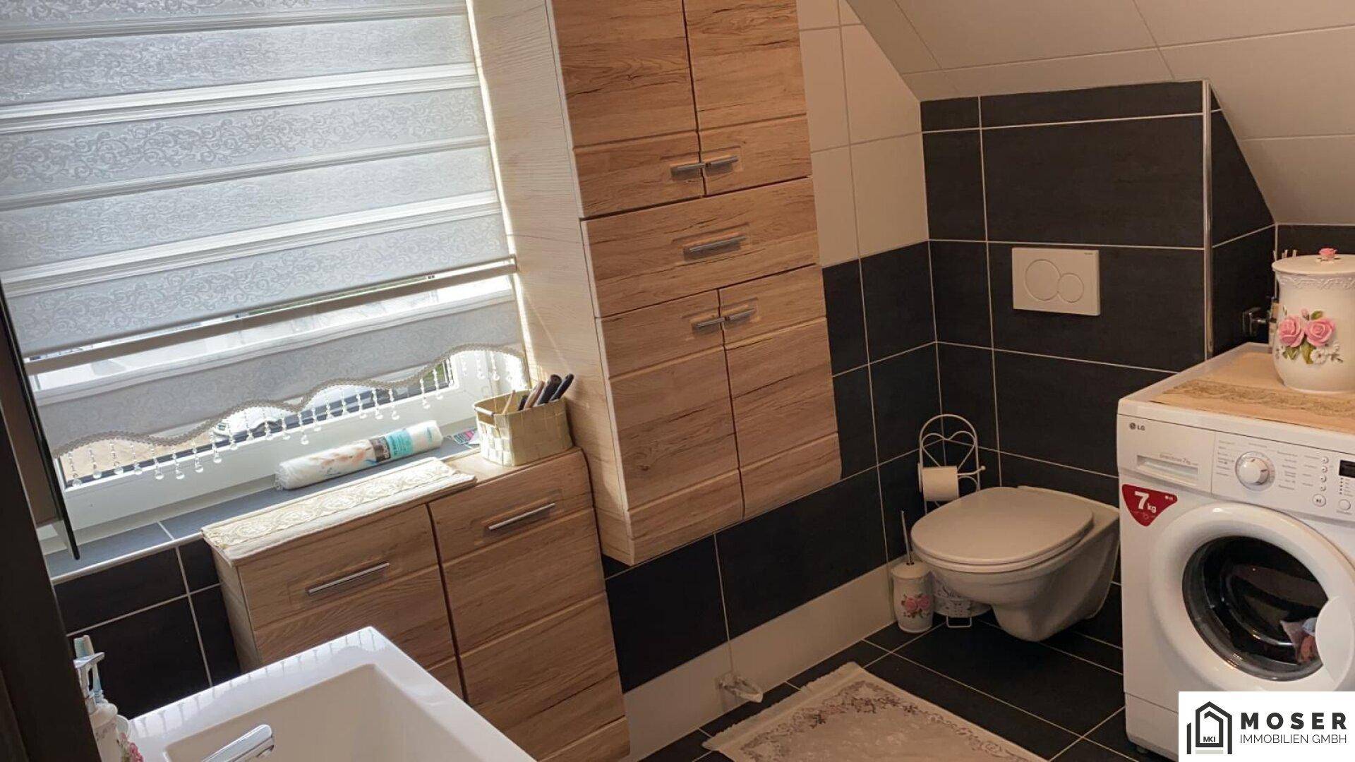 Badezimmer mit Toilette, Waschmaschine und Holzschränken unter einer Dachschräge.