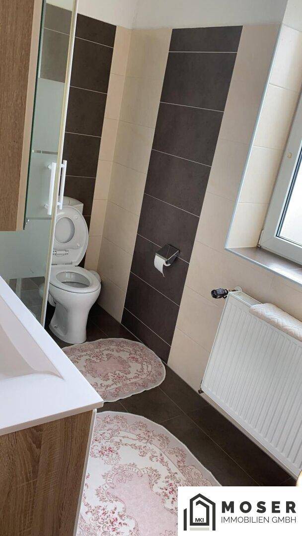 Kleines WC mit Toilette und Heizkörper, gefliest in Beige und Braun.