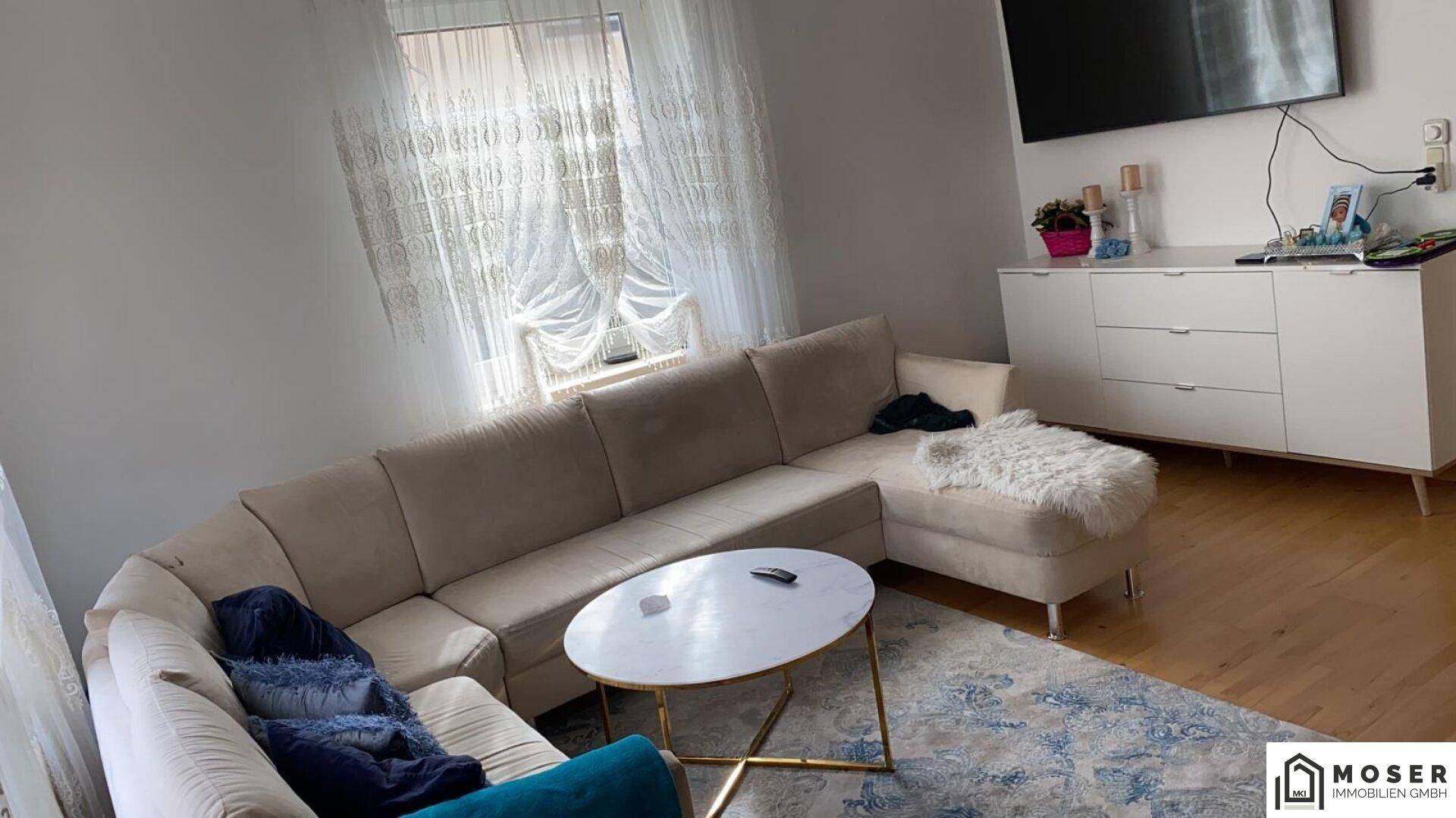 Helles Wohnzimmer mit großem Ecksofa, modernem Couchtisch und Fernseher.