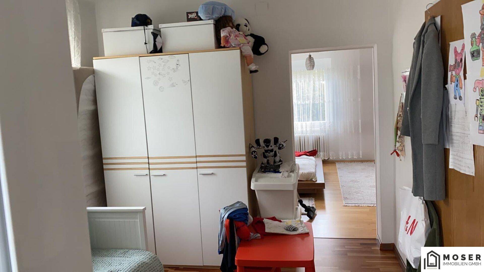 Kinderzimmer mit weißem Kleiderschrank und Blick in einen angrenzenden Raum.