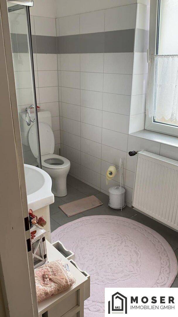 Kleines Badezimmer mit WC, Waschbecken, Duschkabine und Fenster, hell gefliest.