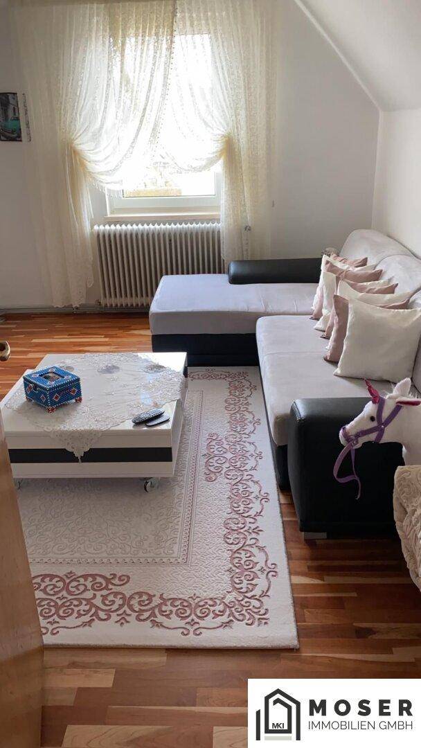 Gemütliches Wohnzimmer mit Ecksofa, Couchtisch und gemustertem Teppich auf Holzfußboden.