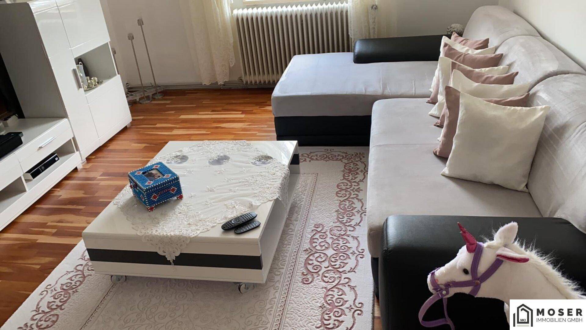Helles Wohnzimmer mit Ecksofa, Couchtisch und weißem Schrank auf Parkettboden.