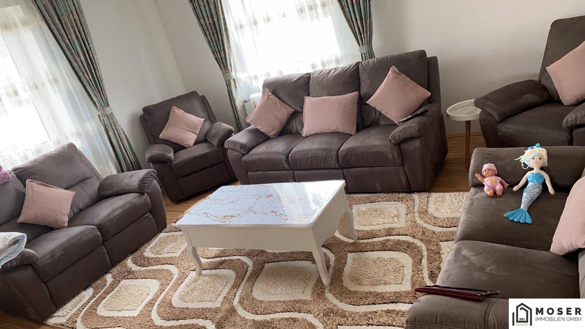 Geräumiges Wohnzimmer mit bequemen Sofas und gemustertem Teppich, hell und einladend.