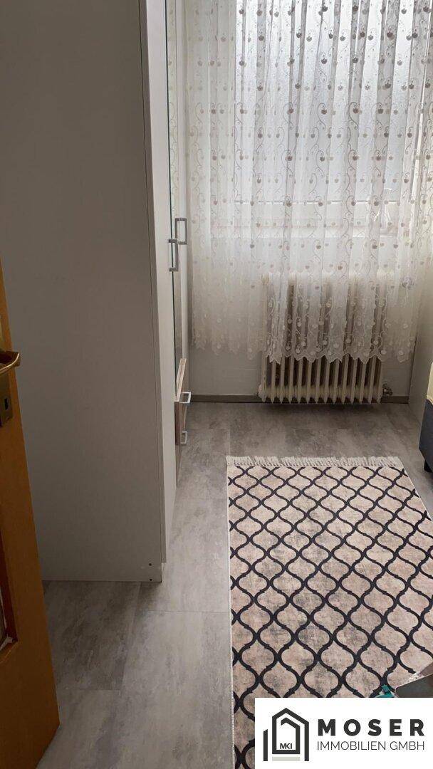 Innenraum mit Schrank und Fenster, ausgestattet mit Vorhängen und Teppich.