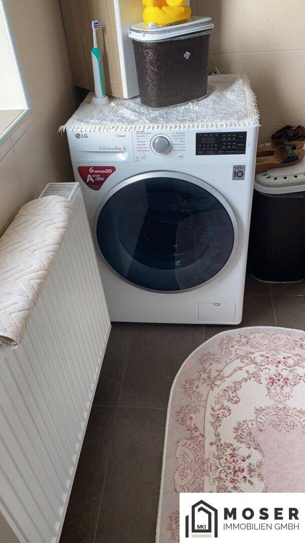 Badezimmer mit Waschmaschine, Heizkörper und Fenster, hell gefliest.