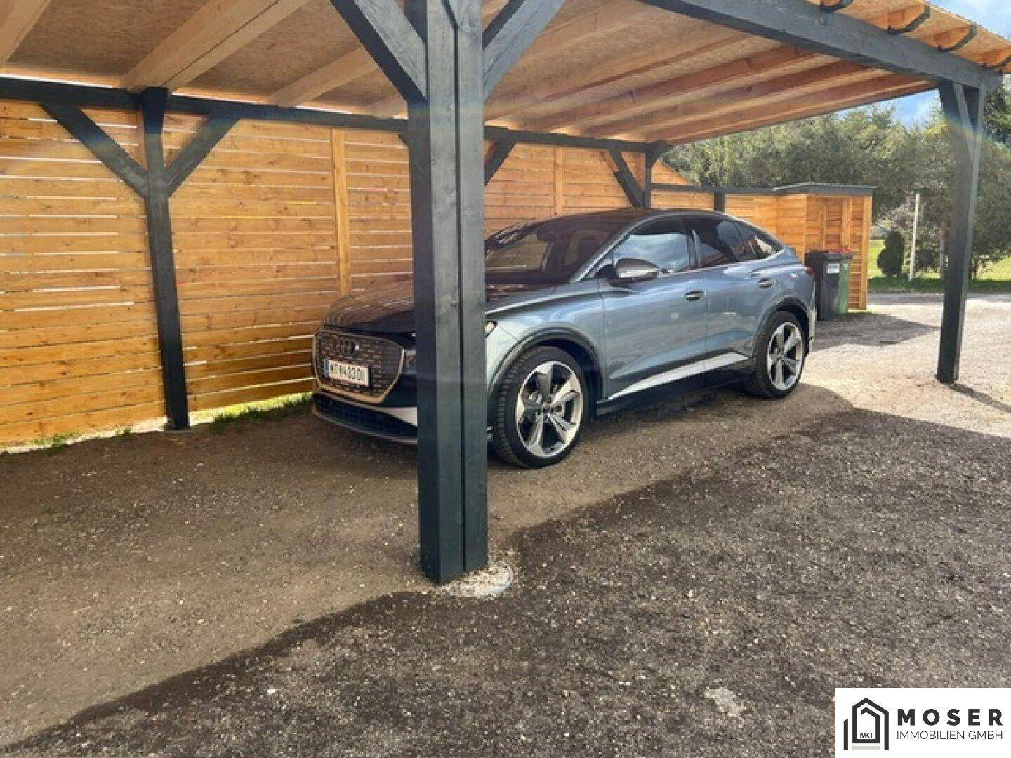 Carport mit Holzkonstruktion und einem geparkten Auto, umgeben von einem Holzzaun.