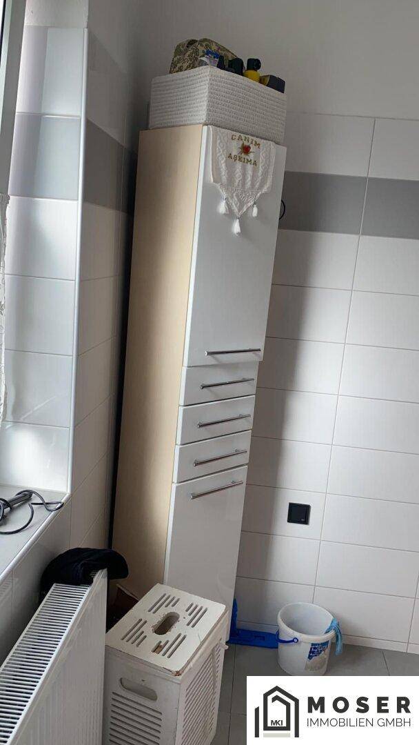 Badezimmer mit hohem Schrank, Heizkörper und Fenster, hell gefliest.