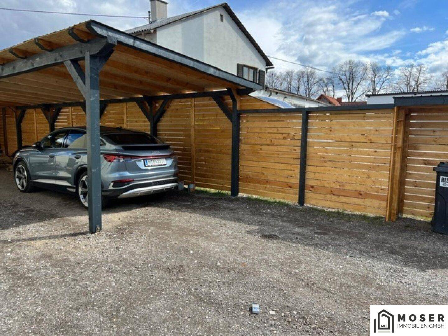 Geräumiger Carport mit Holzzaun und Kiesboden, bietet Schutz für ein Fahrzeug.