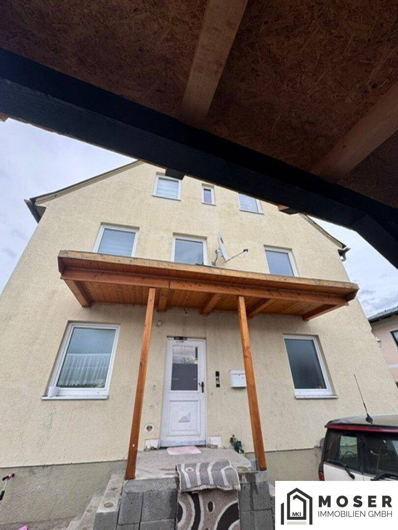 Überdachter Hauseingang mit Holzkonstruktion und weißer Eingangstür.