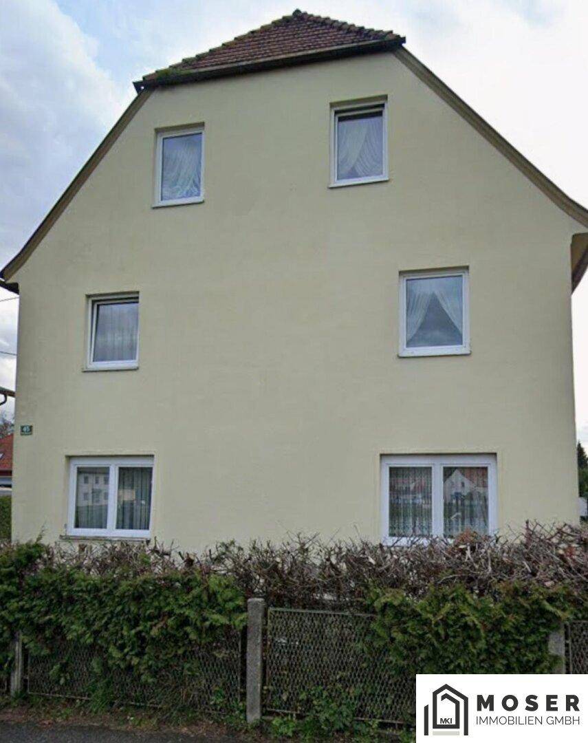 Vorderansicht eines Einfamilienhauses mit beiger Fassade und mehreren Fenstern.