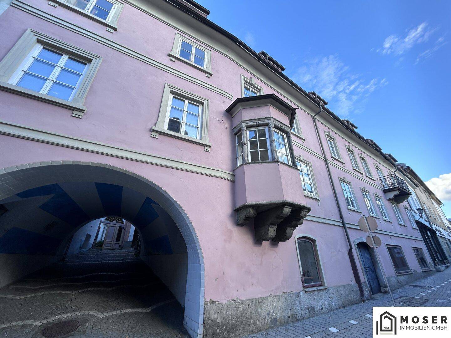 Historisches Gebäude mit rosa Fassade, Erker und einem Durchgang mit Kopfsteinpflaster in der Altstadt.