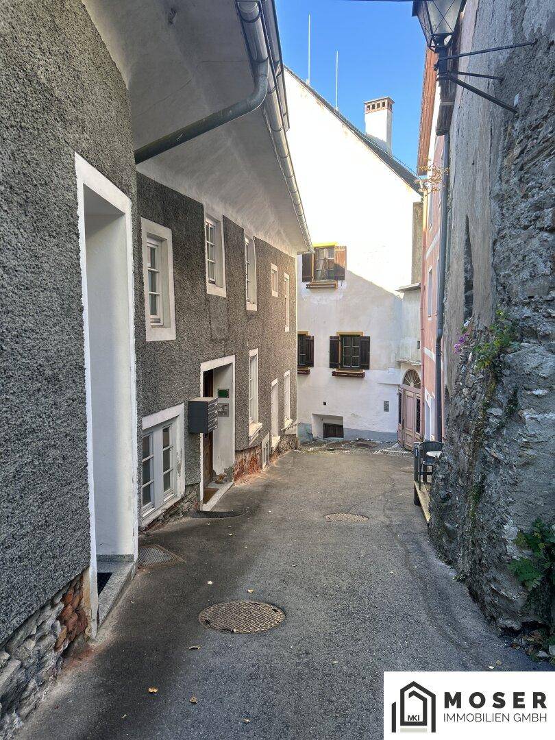Enge Gasse zwischen alten Gebäuden mit rauen Putzfassaden und einem Blick auf den Himmel.