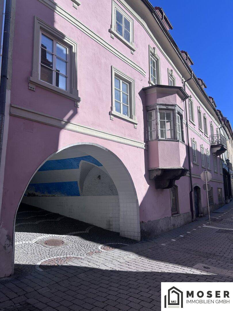 Historisches Gebäude mit rosa Fassade, Erker und einem Durchgang mit Kopfsteinpflaster in der Altstadt.