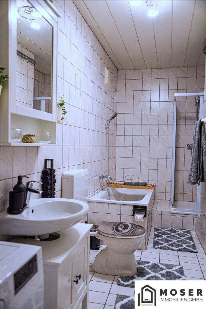 Helles Badezimmer mit weißen Fliesen, Badewanne, Dusche und einem Waschbecken mit Spiegelschrank.