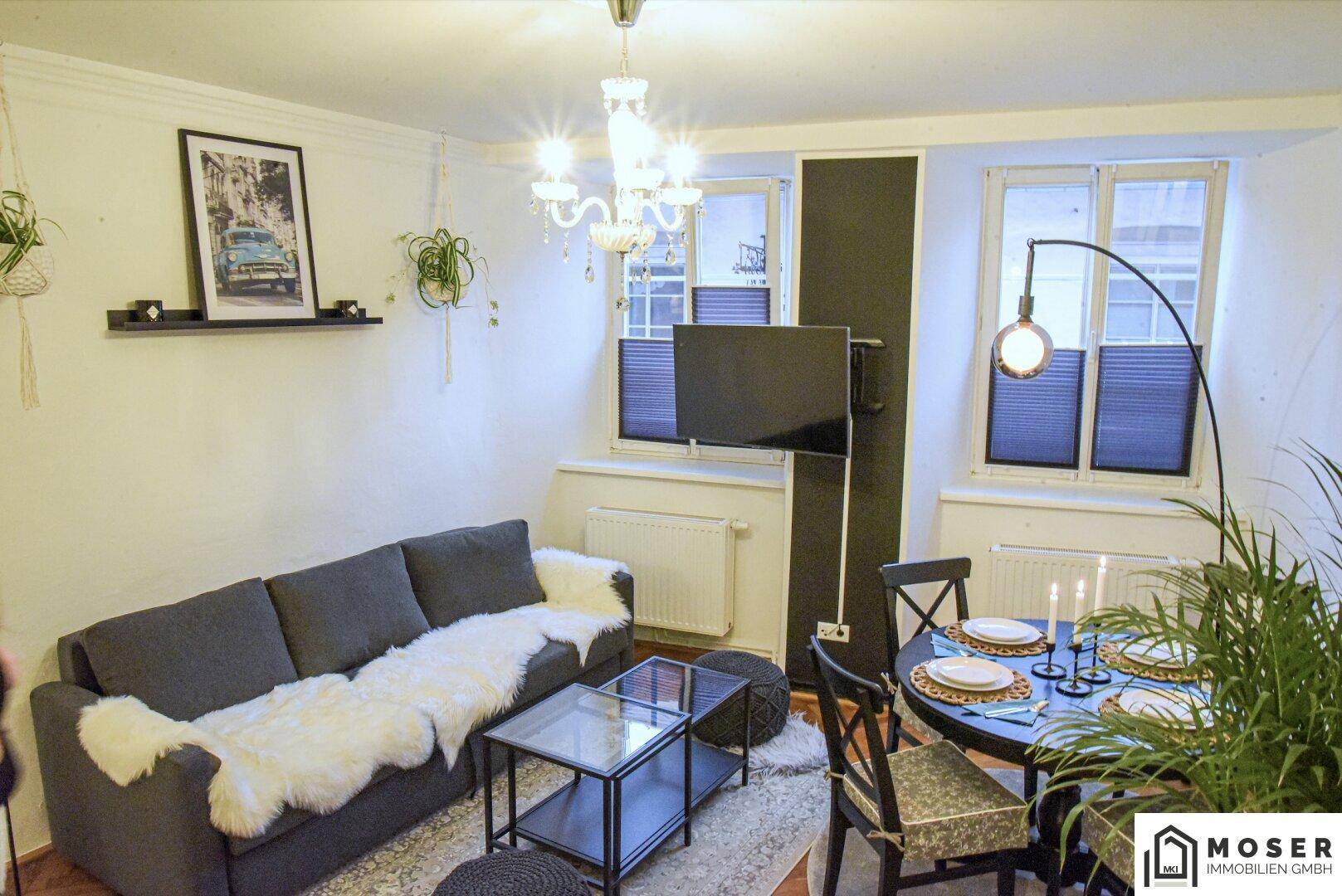 Kombinierter Wohn- und Essbereich mit Sofa, Esstisch und Kronleuchter, hell durch Fenster.