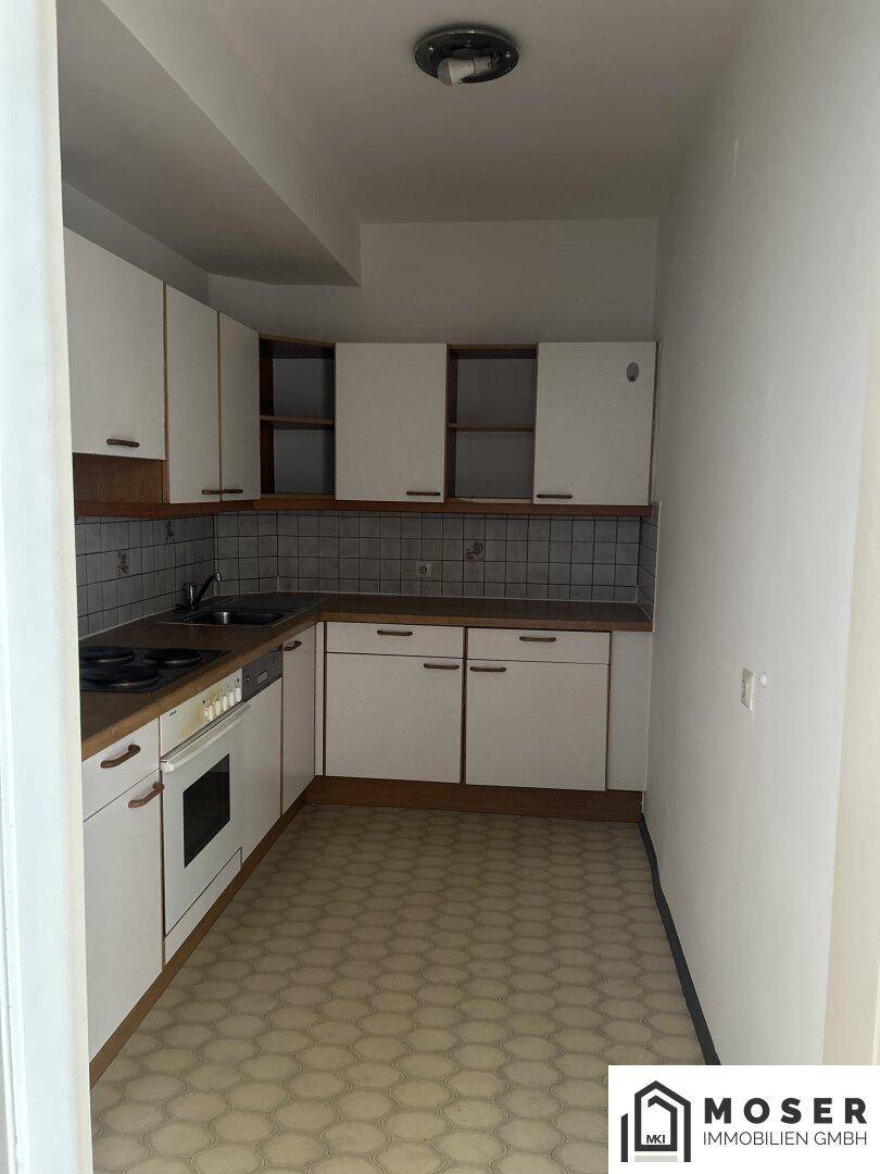 Einfache Küche mit weißen Schränken, Holztheke und gemustertem Linoleumboden.