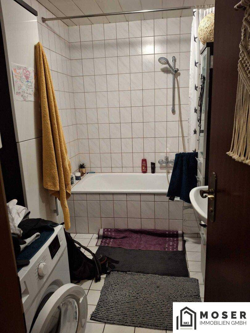 Badezimmer mit Badewanne, Dusche, Waschmaschine und weißen Fliesen, funktional eingerichtet.
