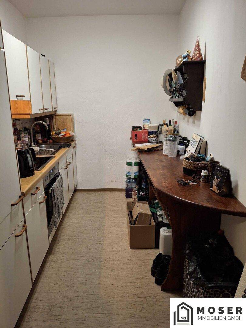 Schmale Küche mit weißen Schränken, Holztheke und einem langen Holztisch.