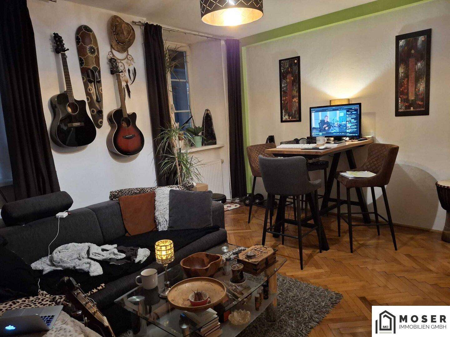Gemütliches Wohnzimmer mit Sofa, Bartisch und Gitarren an der Wand, warm beleuchtet.