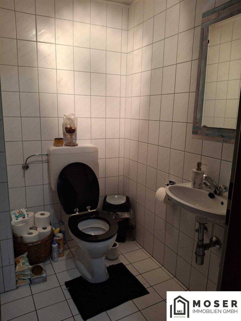 Kleines WC mit weißen Fliesen, Toilette und Waschbecken, funktional eingerichtet.