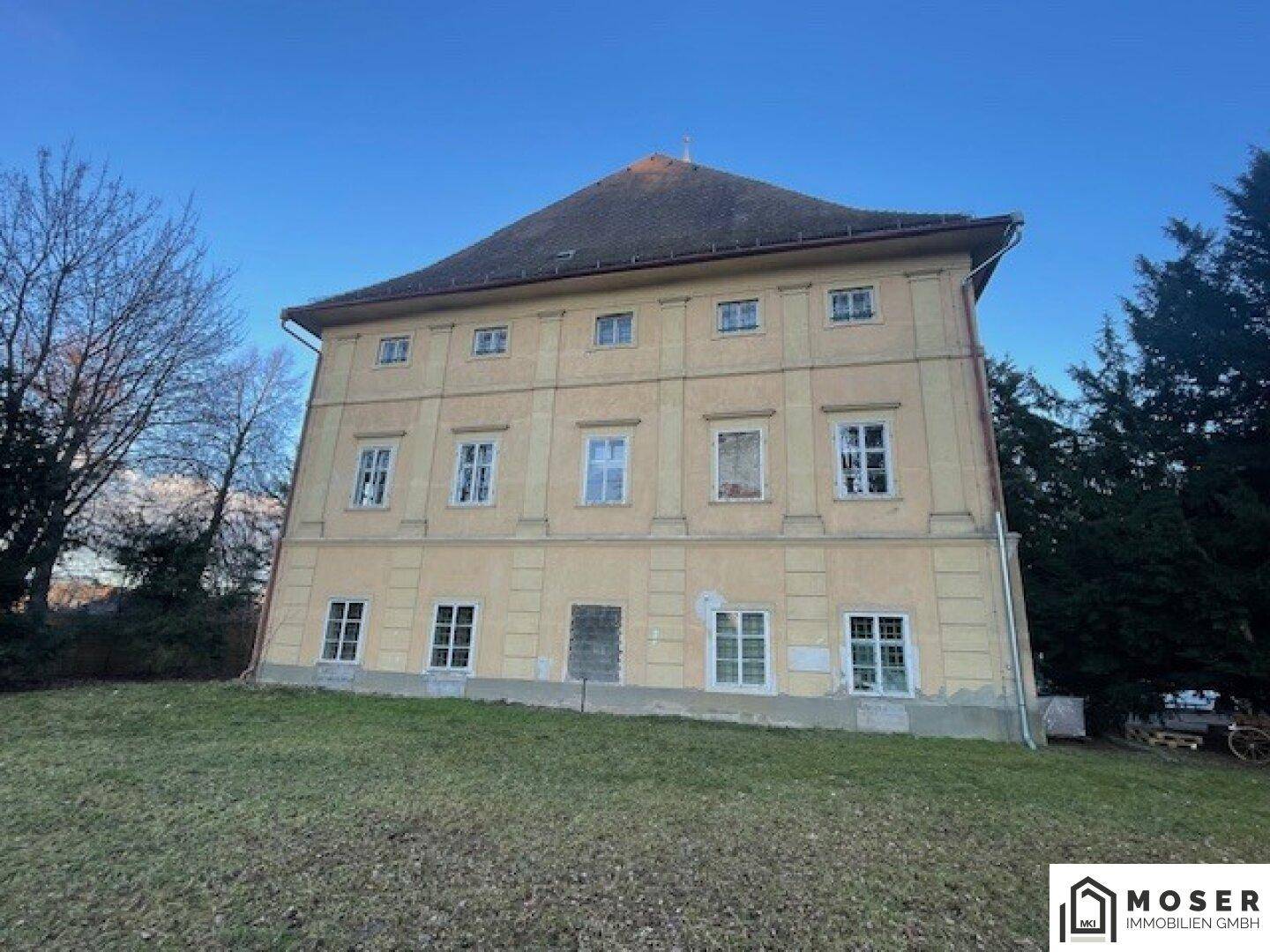 Seitenansicht des historischen Gebäudes mit gelber Fassade und einem großen Rasenbereich im Vordergrund.