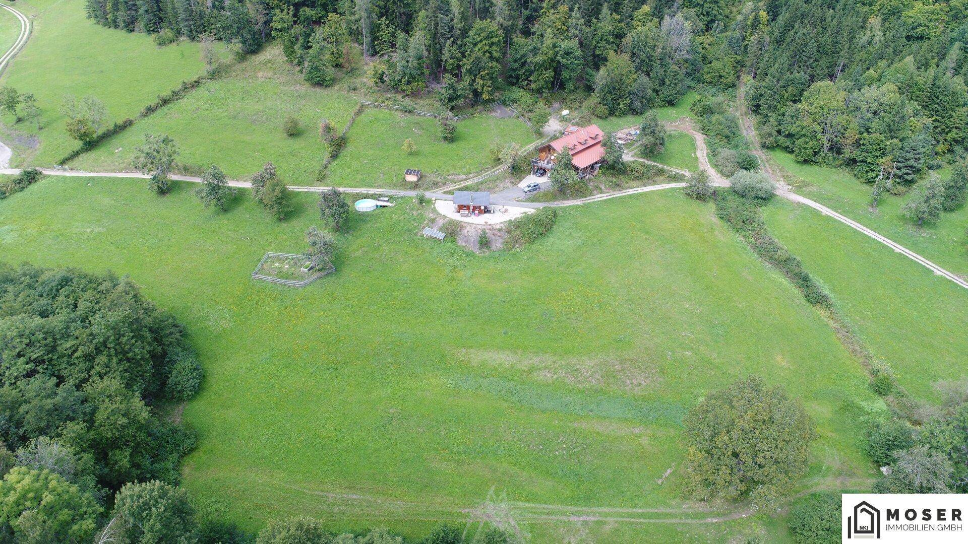 Weitläufige Luftaufnahme des Anwesens mit Haupthaus und Hütte, umgeben von weiten Wiesen und Wäldern.