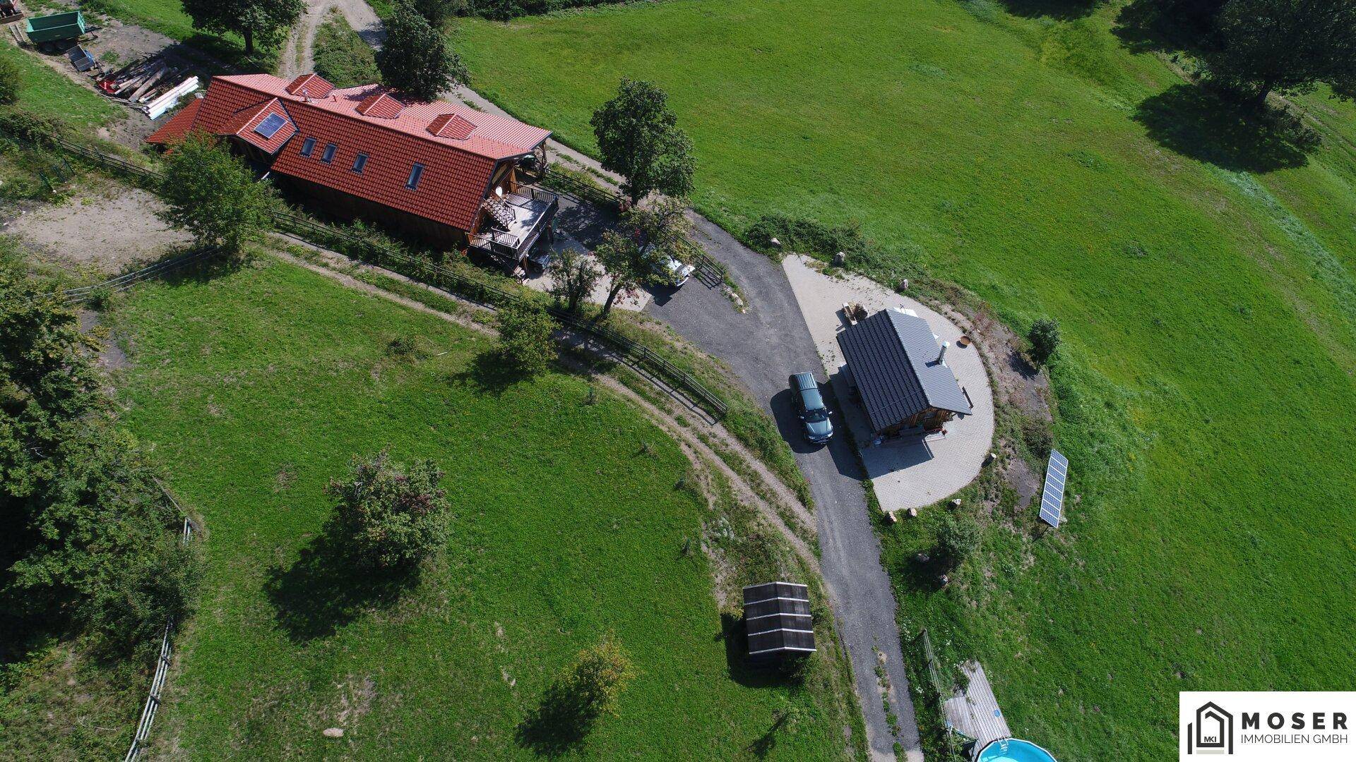 Luftaufnahme von oben auf das Haupthaus und die Hütte, mit Zufahrt, Solarpaneelen und oberirdischem Pool.