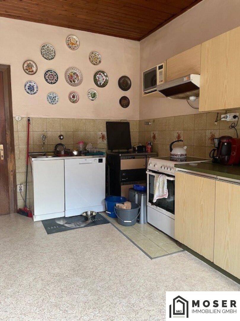 Rustikale Küche mit älteren Einbaumöbeln, Fliesenrückwand und Linoleumboden.