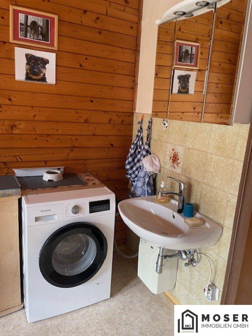 Kleiner Waschraum mit Waschmaschine, Waschbecken und Holzvertäfelung an den Wänden.