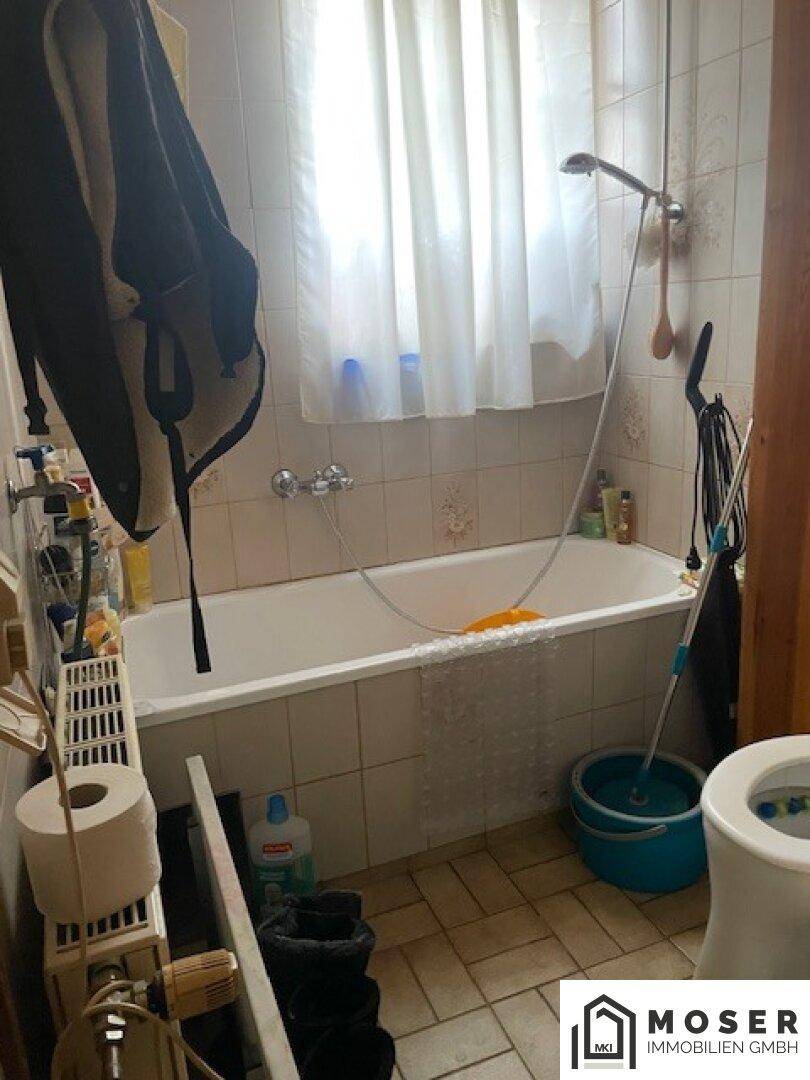 Badezimmer mit Badewanne, Duschvorrichtung und Fliesen im Retro-Stil.