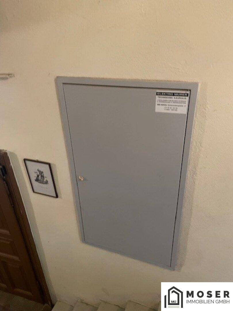 Flur mit einer unscheinbaren Tür und einem Sicherungskasten an der Wand.