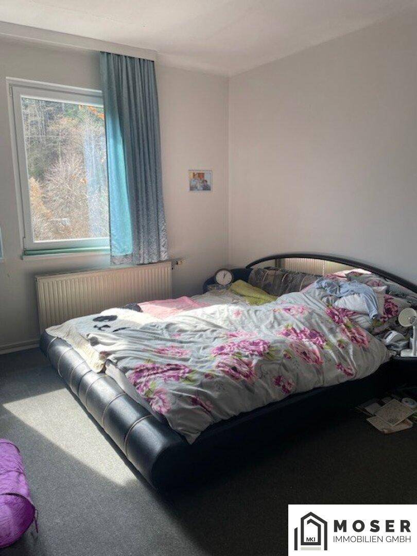 Helles Schlafzimmer mit Doppelbett, Fenster und Blick auf die Umgebung.