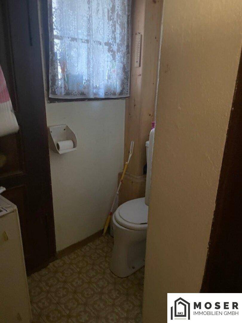 Kleines WC mit Toilette, Fenster und Fliesenboden.