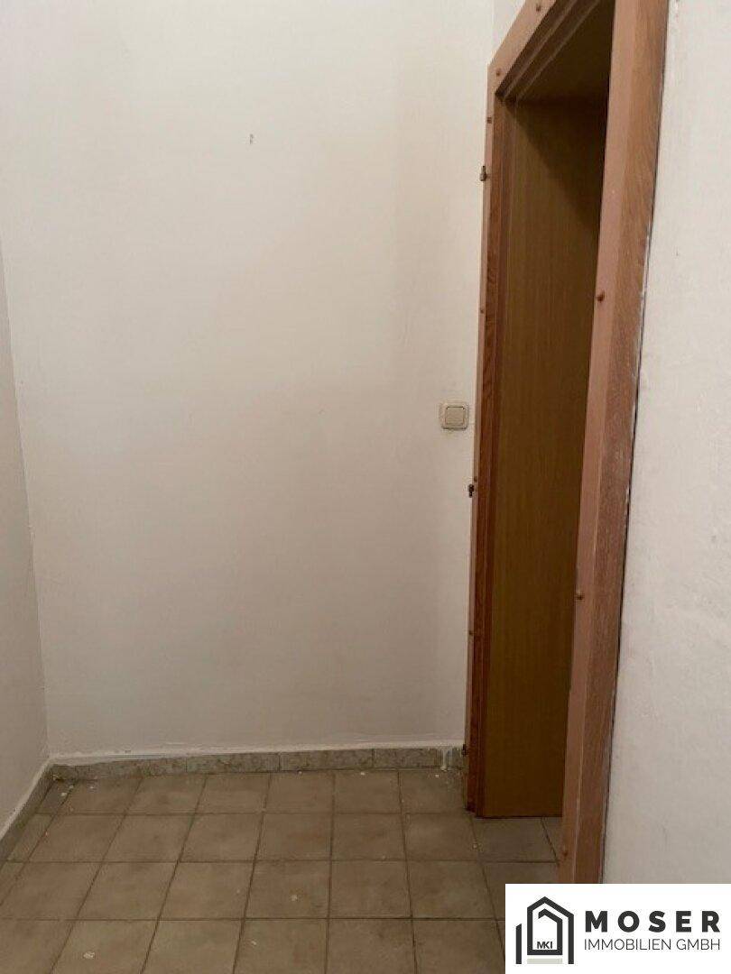 Leerer Flur mit Fliesenboden und einer Holztür, bereit zur Renovierung.