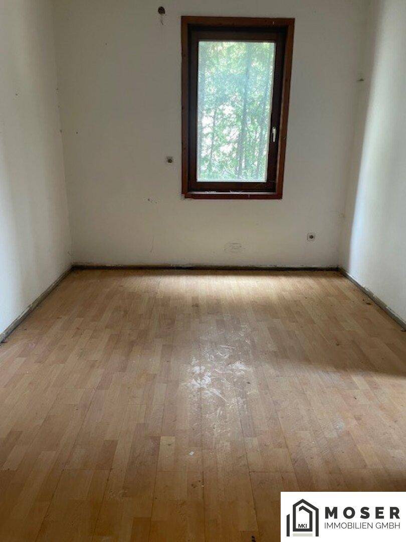 Leeres Zimmer mit Parkettboden und einem Fenster, das viel Licht hereinlässt.