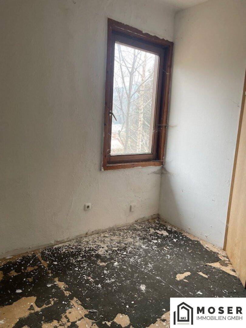 Renovierungsbedürftiges Zimmer mit beschädigtem Boden und einem Fenster.