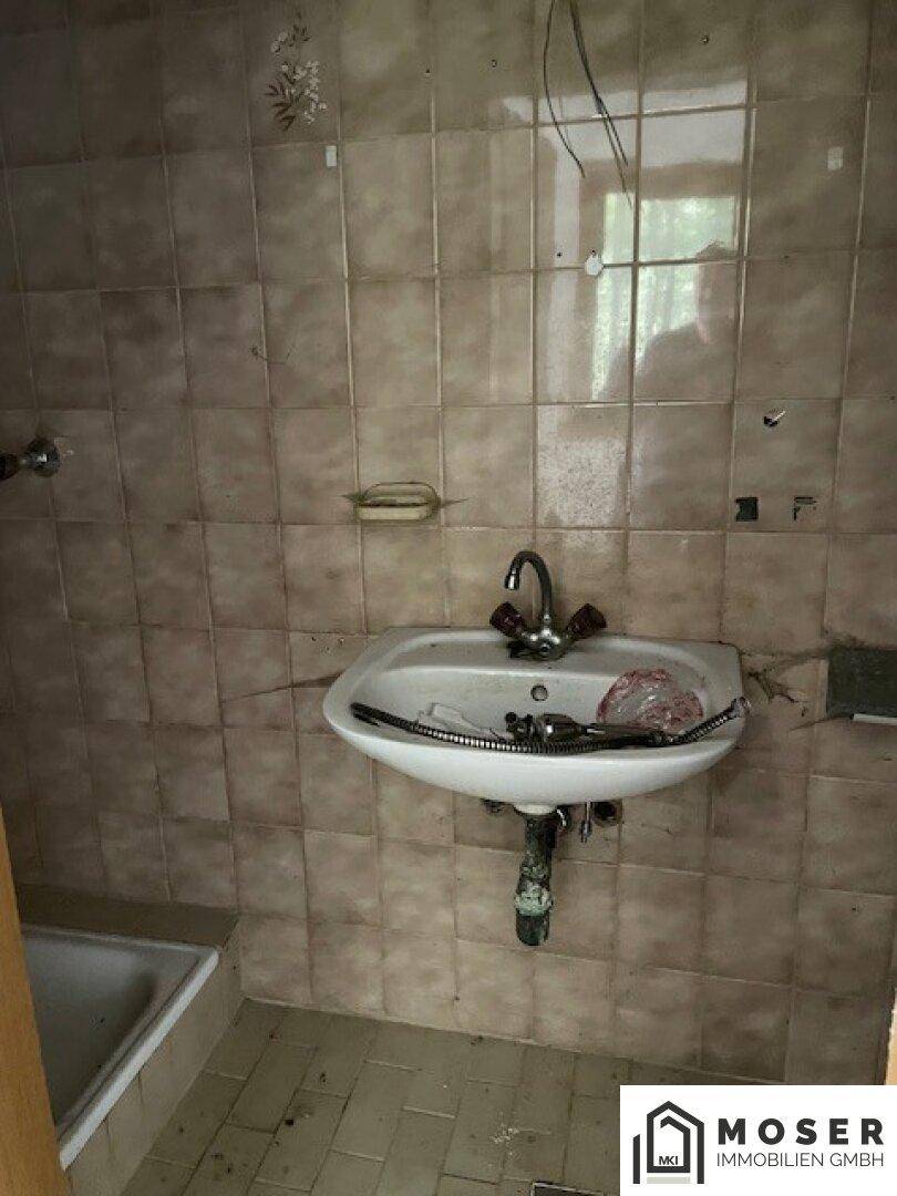 Badezimmer mit Waschbecken und älteren Fliesen, das eine Renovierung benötigt.