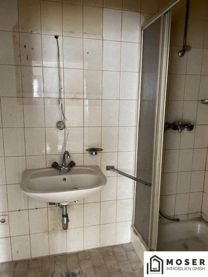 Badezimmer mit Waschbecken und Duschkabine, umgeben von braunen Fliesen.