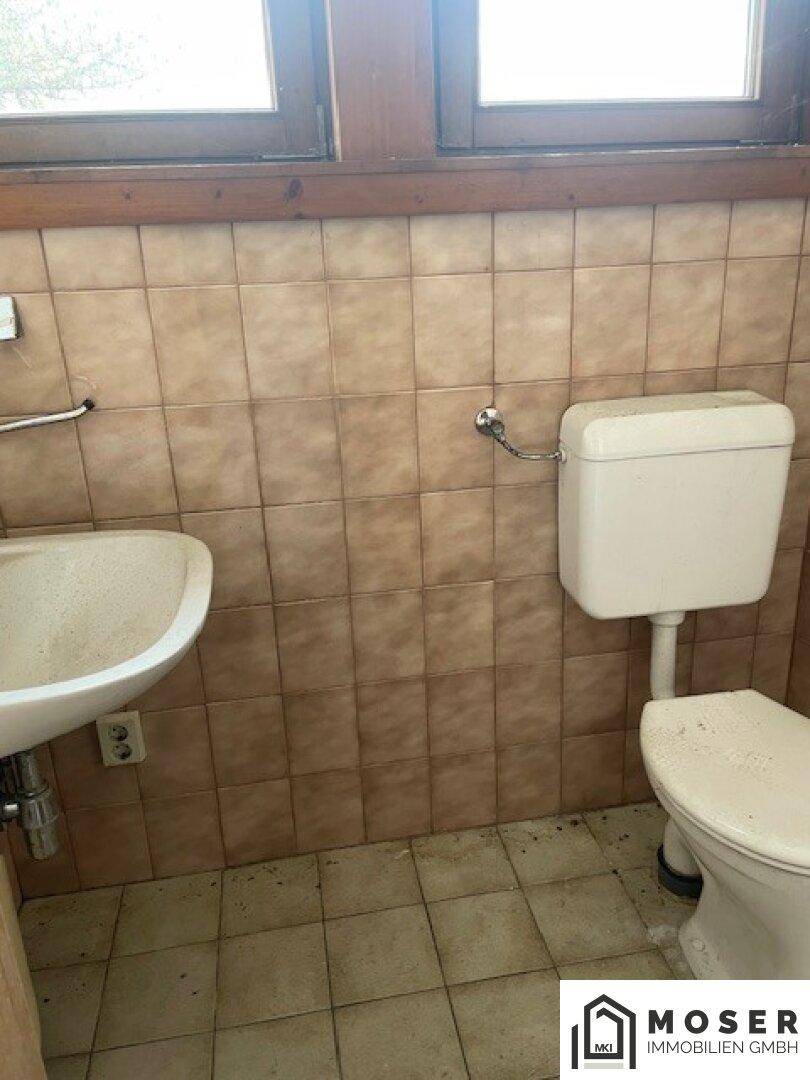 WC mit Waschbecken, Toilette und Fenster, umgeben von braunen Fliesen.
