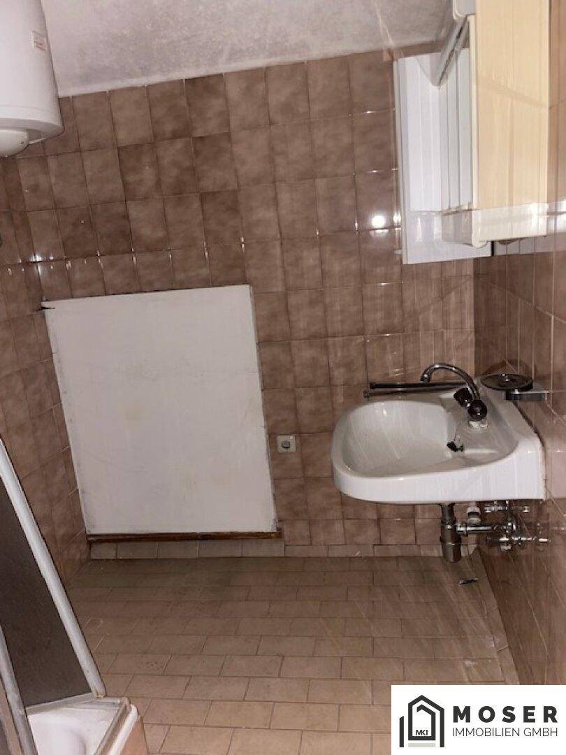 Badezimmer mit Waschbecken und braunen Fliesen, das eine Modernisierung benötigt.