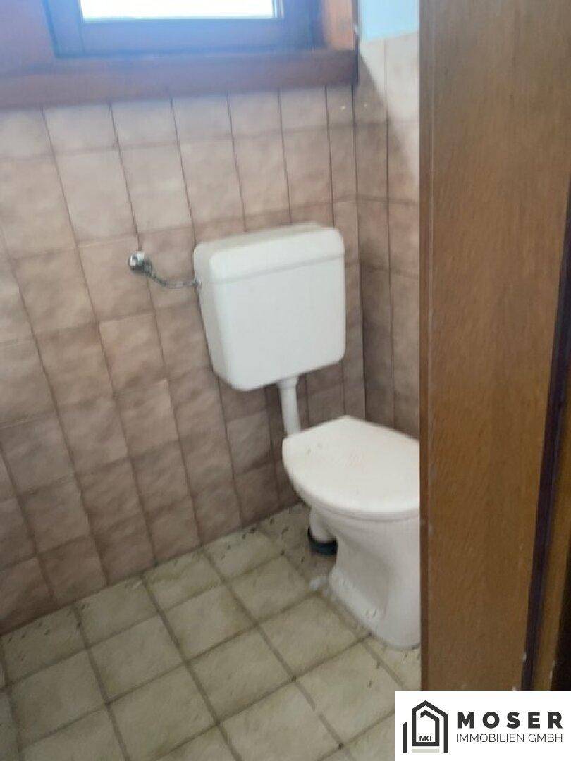 Kleines WC mit Toilette und braunen Fliesen, bereit für eine Renovierung.