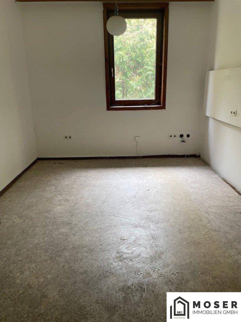 Renovierungsbedürftiges Dachzimmer mit beschädigtem Boden und einem Fenster.