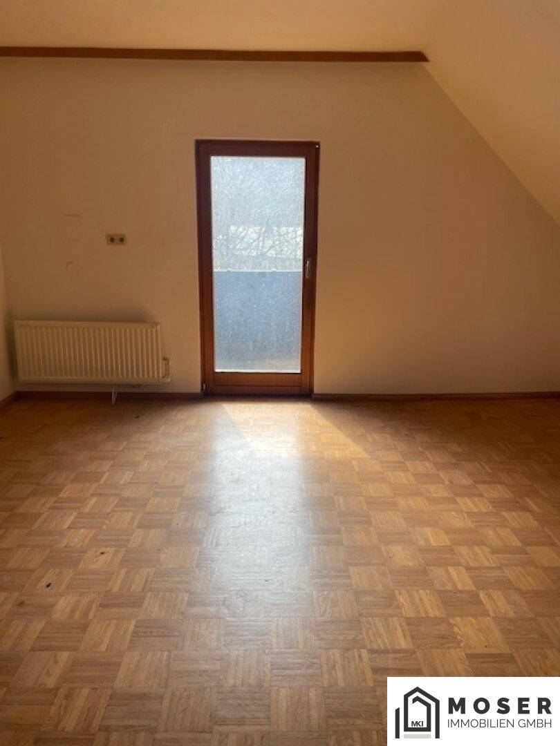 Helles Dachzimmer mit Parkettboden und einer Tür, die ins Freie führt.