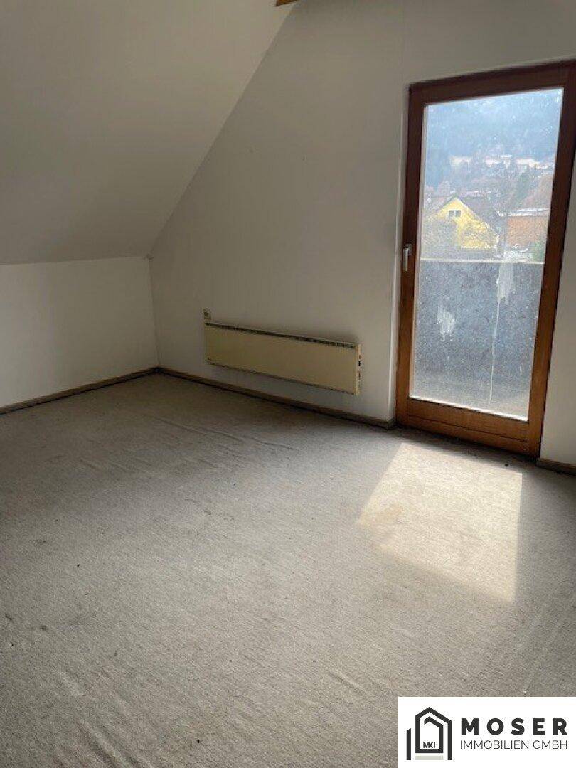 Dachzimmer mit Teppichboden, schrägen Wänden und einem Fenster mit Ausblick.