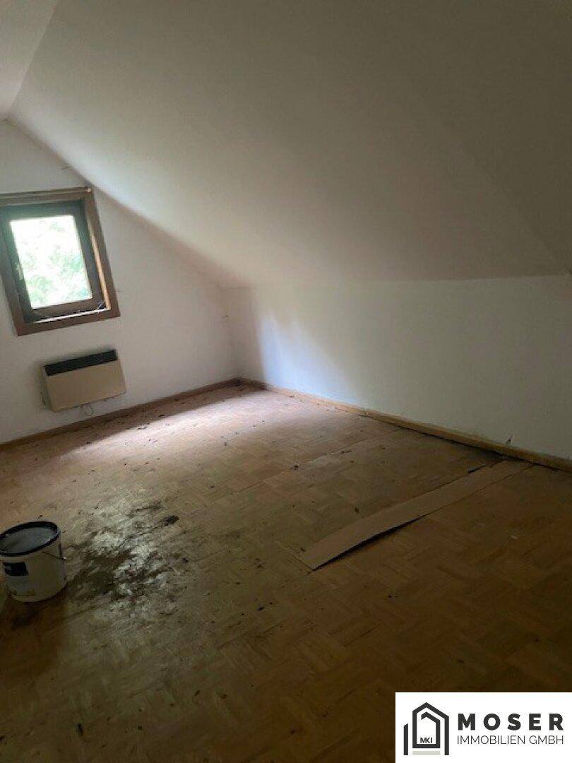 Dachzimmer mit Parkettboden, schrägen Wänden und einem kleinen Fenster.