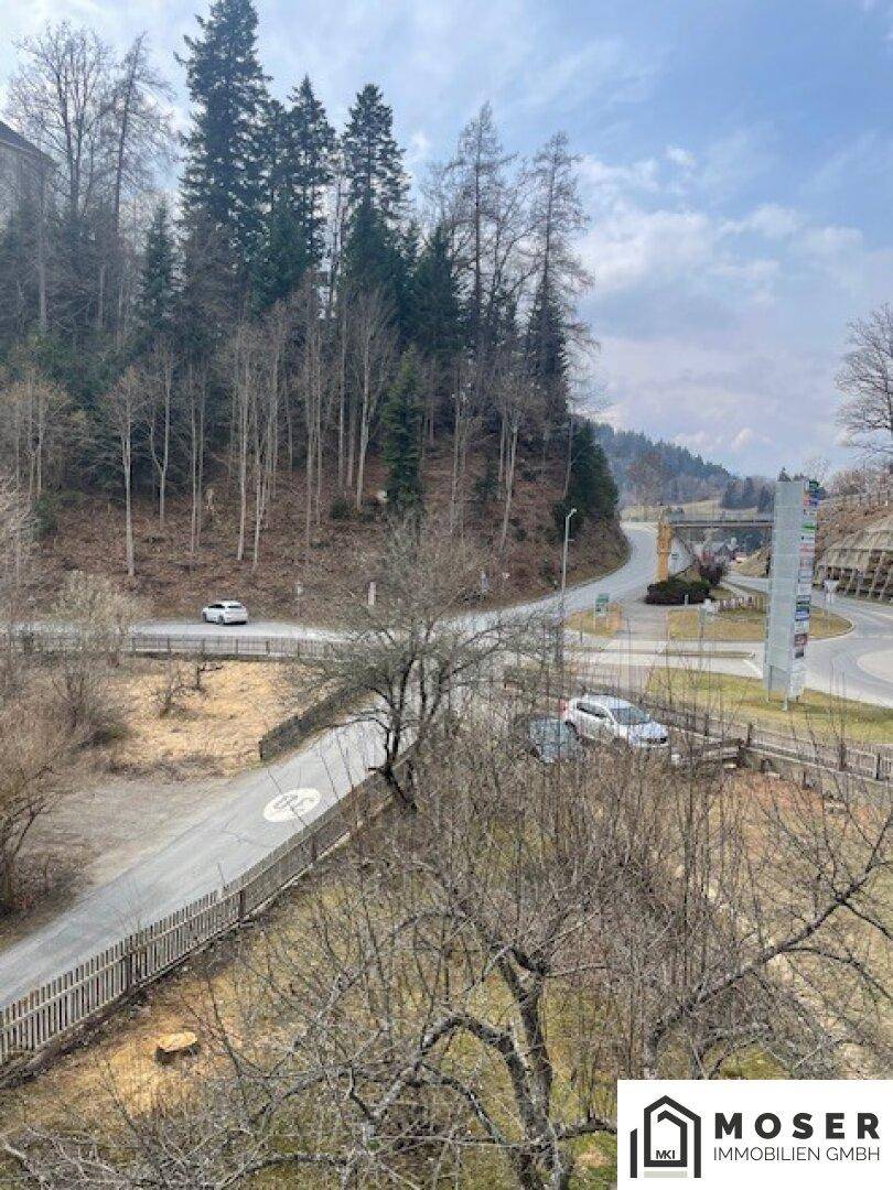 Panoramablick auf eine Straße mit Kreisverkehr und bewaldeten Hügeln im Hintergrund.