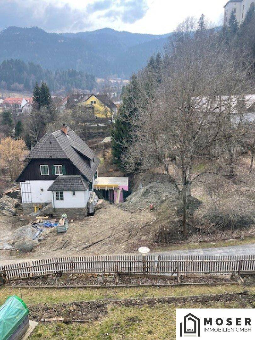 Blick auf ein Haus in Renovierung mit Bergkulisse und umliegender Natur.